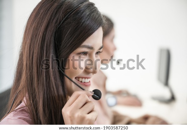 Portrait of beautiful asian woman sitting\
smiling and wearing headset working customer support and assistance\
service call center in workplace at office. Business call center\
and hot line\
operators.