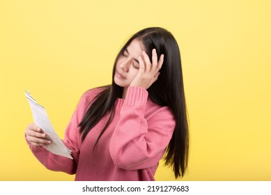 Portrait of a beautiful Asian woman, stressed, tired, holding a bill spreadsheet in her hand. A woman's problem that she worries about the bill. Studio photography isolated on pink background.