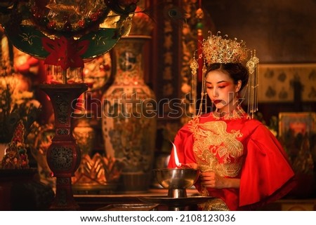 portrait of beautiful asian woman in traditional Chinese dress in Chinese shrine lighting candle to worship Chinese god in Chinese new year festival celebration
