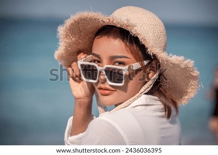 Portrait beautiful Asian woman wearing Bikini ,white t-shirt, sunglasses and straw hat at beach on vacation looking away while enjoying sea breeze is summer vacation concept.