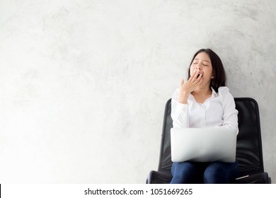 Portrait Of Beautiful Asian Young Woman Yawn At Her Work Place With Laptop Computer On Cement Background, Girl Working Freelance Is A Blogger With Stress And Tired, Copy Space. 