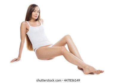 Portrait of beautiful attractive Caucasian young model with long legs sitting against white background and looking at camera. Smiling person posing in tank top and panties. Horizontal studio shot