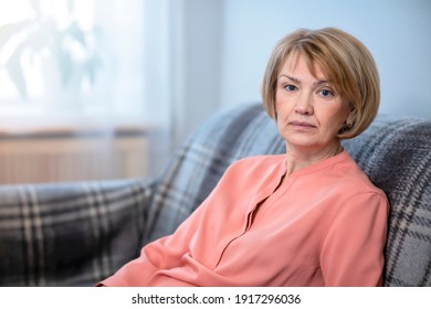 Portrait Of Beautiful Attractive Woman, Adult Elderly Senior Mature Lady Sitting On Couch At Home In Living Room And Looking At Camera With A Serious Look