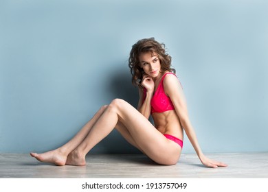 Portrait of a beautiful attractive woman in pink lingerie sitting on the floor near a blue wall. Studio shot.