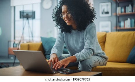 Portrait Of A Beautiful Authentic Latina Female In A Stylish Cozy Living Room Using Laptop Computer At Home. She's Browsing The Internet And Checking Videos On Social Networks And Having Fun.