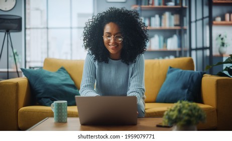 Portrait Of A Beautiful Authentic Latina Female In A Stylish Cozy Living Room Using Laptop Computer At Home. She's Browsing The Internet And Checking Videos On Social Networks And Having Fun.