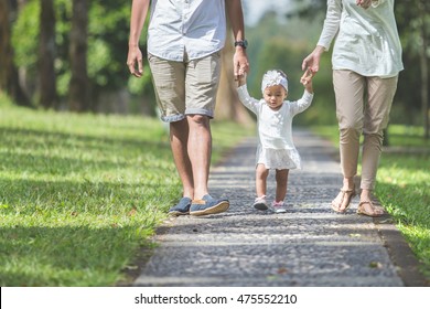 Portrait Of Beautiful Baby Learn To Walk For The First Time With Her Parents Hold Her Hands