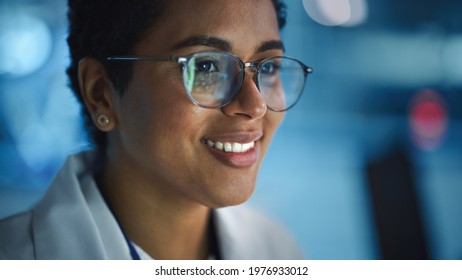 Portrait Of Beautiful Black Latin Woman Computer Screen Reflecting In Her Glasses. Young Intelligent Female Scientist Working In Laboratory. Background Bokeh Blue With High-Tech Technological Lights