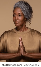 Portrait Of Beautiful Black Woman In Her Late 50s Posing With Her Hands Together Praying On Neutral Background