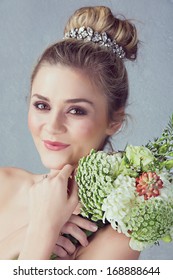 Portrait Of A Beautiful Blond Bride With A Diamante Headpiece. Hair In Romantic Top Knot Bun Hairstyle. Wedding Flowers. 