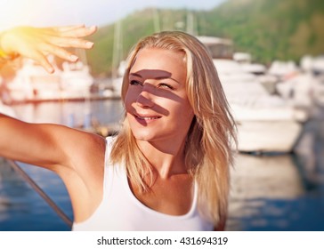 Portrait of a beautiful blond girl covering face by hand of bright sun light, spending weekend on the yacht, happy summer vacation
