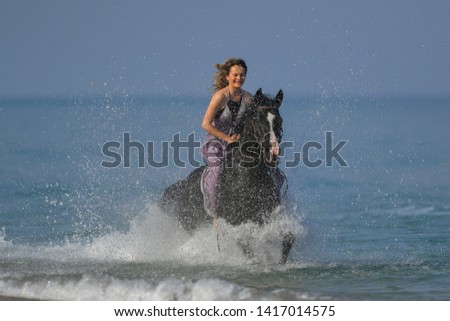 Portrait of a beautiful blond girl  galloping on horseback, dissecting waves on the sea beach