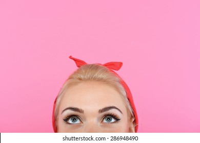 Portrait of a beautiful blond pin up girl with ponytail and red bandana and lipstick looking up, close up photo, isolated on pink background
