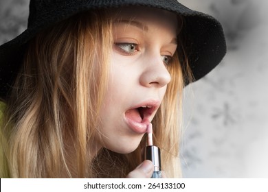 Portrait of beautiful blond teenage girl in black hat doing make up with liquid lipstick