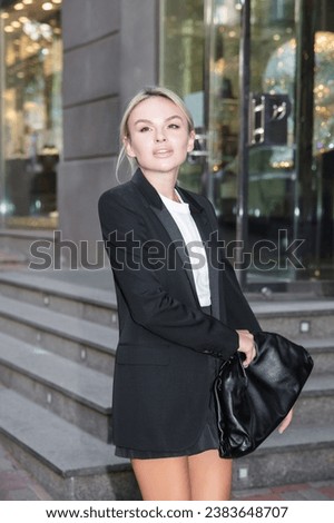 Portrait of a beautiful blonde dressed in a black suit posing on the street