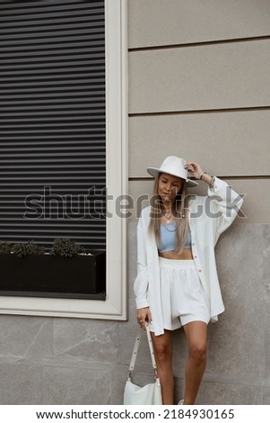 portrait of beautiful blonde girl dressed in white linen suit, oversized shirt, shorts, blue top, sandals, hat, bag, accessories, stylish trendy summer fashion outlook, lifestyle model