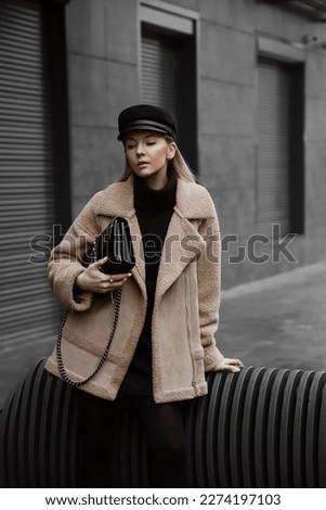 portrait of beautiful blonde girl dressed in black tights, skirt, knitted turtleneck, massive boots, cap, bag in hand, beige sheepskin coat, accessories, stylish fashion outfit, lifestyle model