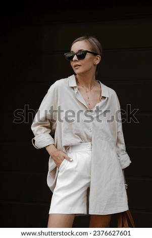 portrait of beautiful blonde girl dressed in linen beige shirt, white shorts, straw bag, accessories, sunglasses, hair gathered, stylish fashion outfit, lifestyle model