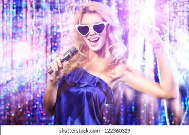 Portrait of a beautiful blonde girl singing with a microphone. Disco lights in the background.