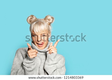 Portrait of beautiful blonde girl wearing cozy grey sweater and making faces. Pretty model in cheerful mood posing on blue background. Copy space in right side. Winter and emotion concept