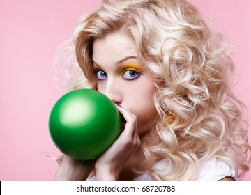 portrait of beautiful blonde party girl blowing up green balloon