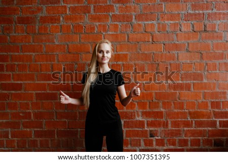 Portrait of beautiful blonde  woman in black sportswear standing against the background of a red brick wall after fitness workout.Fites concept. The girl poses, the place for copy spase nearby