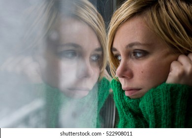 Portrait Of A Beautiful Blonde Woman With Green Warm Sweater Reflected In A Glass Window Looking Outside