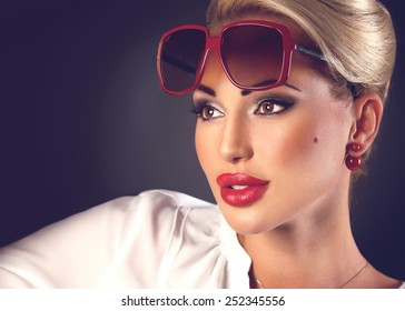 Portrait of beautiful blonde woman in sunglasses and red plump lips on dark background with copyspace