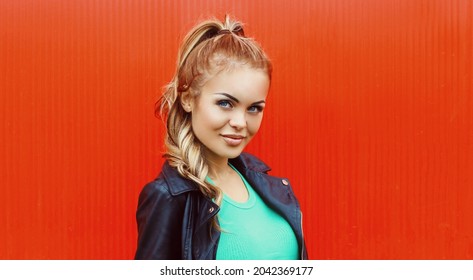 Portrait of beautiful blonde young woman wearing a black rock jacket on red background