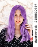 Portrait of a beautiful blue-eyed woman with purple hair looking into the camera against a light marble wall. Hair dyeing, coloring. Hair care, hairdressing, trichology
