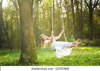 Portrait of a beautiful bride in white wedding dress smiling and swinging in the forest