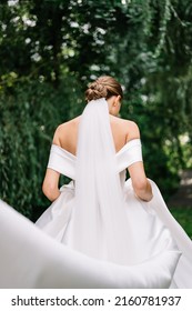 Portrait of beautiful bride in white wedding dress with modern hairstyle and veil walking on garden, back view. Wedding concept