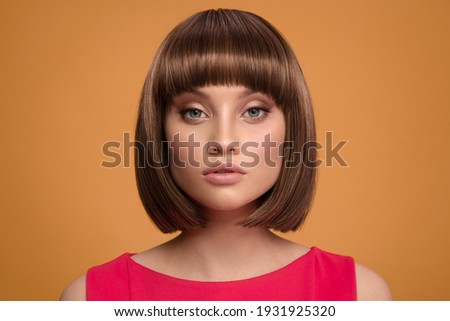 Portrait of a beautiful brown-haired woman with a short haircut on a yellow background.