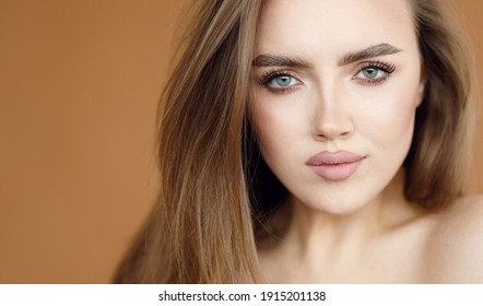 Portrait of a beautiful brunette with clear skin and expressive eyes. Beauty portrait of a girl with natural makeup on a brown background.
