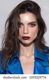 Portrait Of A Beautiful Brunette Girl With Hazel Eyes And Square Jaw And Chin. Perfect Skin, Dark Red Lips, Blue Coat.