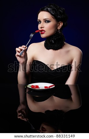 portrait of beautiful brunette girl posing with fork and single red hot spicy cayenne on white plate