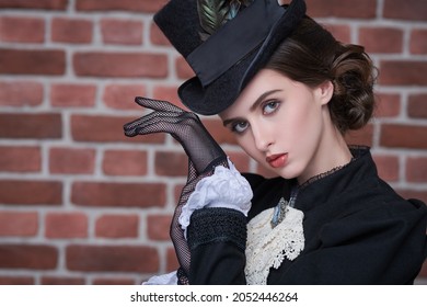 Portrait of a beautiful brunette lady with makeup, hairstyle and clothes of the 19th century in the background of a brick wall. Historical hairstyle and makeup.