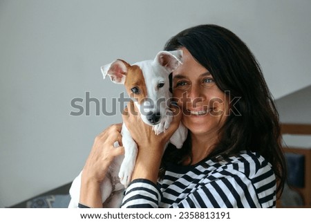 Portrait of a beautiful brunette mid adult woman playing with her adorable jack russell terrier puppy. Loving owner and her funny looking dog having fun. Background, close up, copy space.