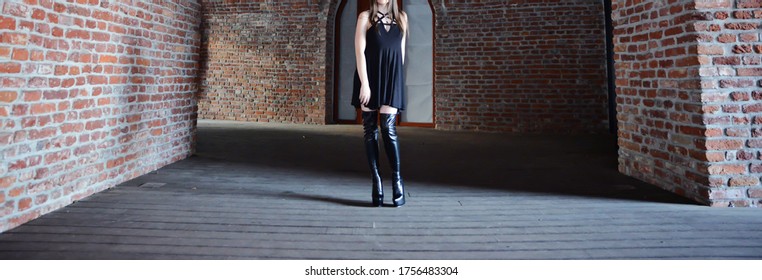 Portrait Of A Beautiful Brunette Woman. The Model Is Wearing A Short Black Skirt And Knee High Leather Boots. High Heels