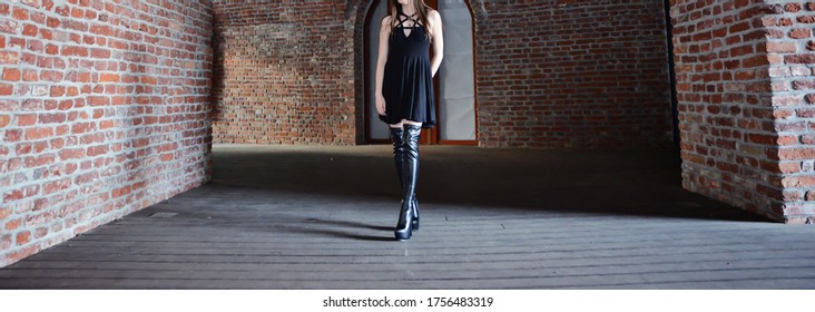 Portrait Of A Beautiful Brunette Woman. The Model Is Wearing A Short Black Skirt And Knee High Leather Boots. High Heels