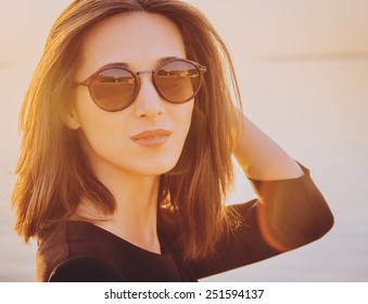 Portrait Of Beautiful Brunette Woman In Round Sunglasses On Beach At Sunny Day. Image With Sunlight Effect