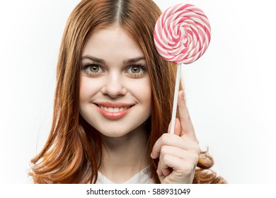 portrait of a beautiful brunette woman smiling  on a white background holding a lollipop in her hand .