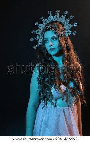 portrait of beautiful brunette woman wearing ornate silver crown headdress, posing with arm gestures, conjuring  magical spell. isolated on dark studio background, cinematic blue moonlight lighting.