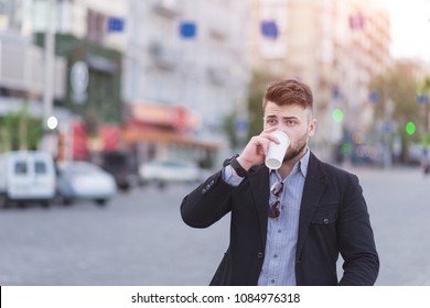 Portrait of a beautiful business man drinking coffee in the background of a blurred urban landscape. - Shutterstock ID 1084976318
