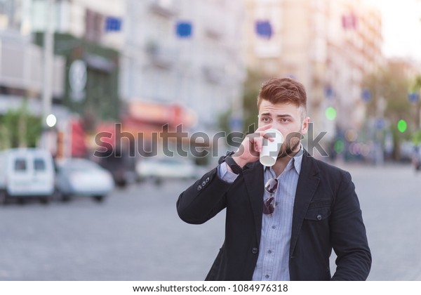 Portrait of a beautiful business\
man drinking coffee in the background of a blurred urban\
landscape.