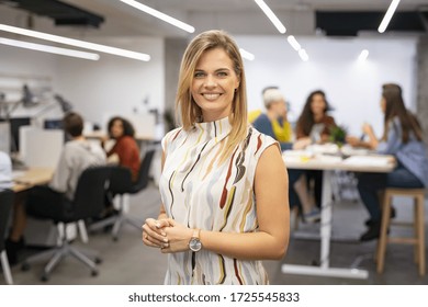 Portrait Of Beautiful Business Woman Looking At Camera While Business Team Working In Background. Executive Woman Standing In Office. Happy And Smiling Creative Businesswoman With Co-workers.