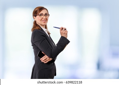 Portrait Of A Beautiful Businesswoman 50 Years Old With Mobile Phone And Pen In The Office.