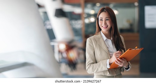 Portrait of beautiful businesswoman holding file folder, smiling and looking away outside while standing in office room. - Powered by Shutterstock