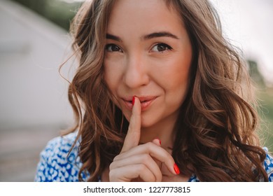 Portrait Beautiful Caucasian Woman Brunette Holding An Index Finger At Her Lips, Asking To Keep Her Silence Or Not Tell Anyone Her Mystery, Looking At Camera , Saying 