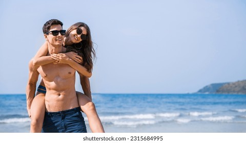 Portrait of beautiful caucasian woman with man wearing sunglasses swim suit piggy back on beach. Young couple enjoy honeymoon after marriage sea. Happy casual lover hold at the tropical beach - Powered by Shutterstock